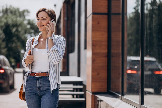 Young woman with phone and computer walking outside the street