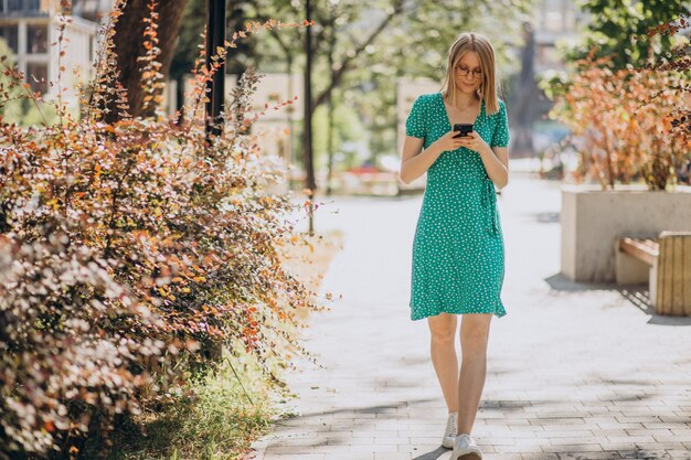 Молодая женщина с телефоном гуляет по улице