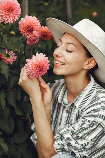 ピンクの花を持つ若い女性。帽子の女性。庭の女の子。