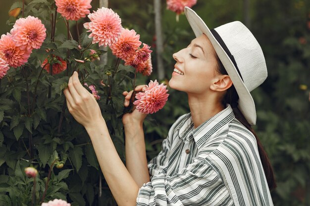 ピンクの花を持つ若い女性。帽子の女性。庭の女の子。