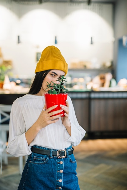 カフェで顔の近くの鍋に植物を持つ若い女