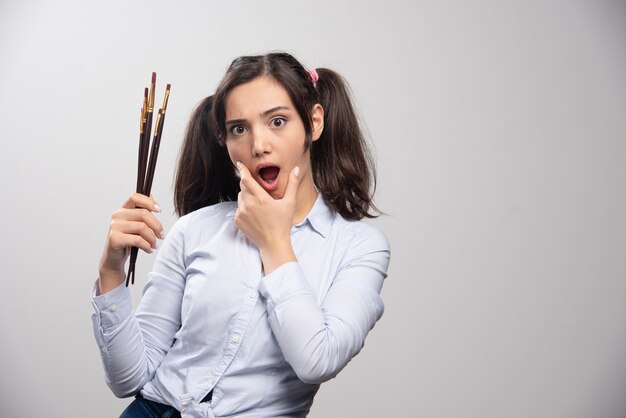 Young woman with ponytail hairstyle holding paintbrushes. 