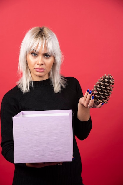 Free photo young woman with present holding a big pinecone on a red background. high quality photo