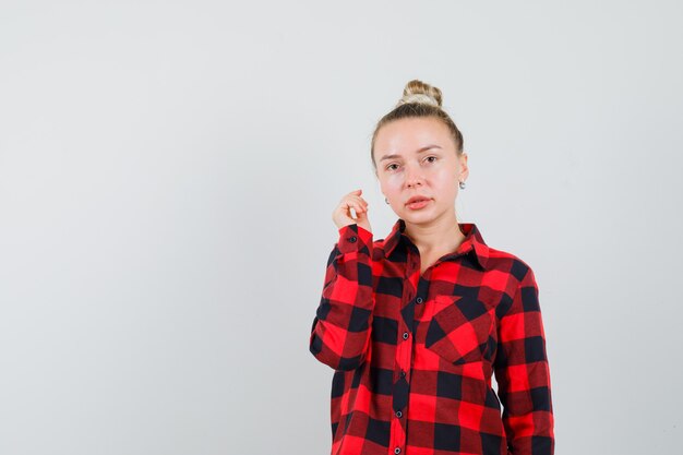 Young woman with raised arm in checked shirt and looking sensible