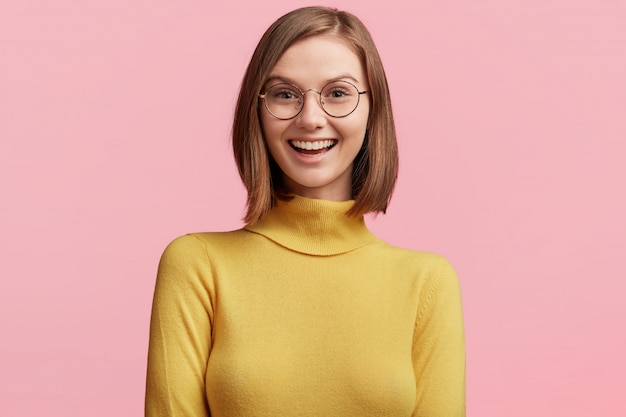 丸いメガネと黄色のセーターを持つ若い女性