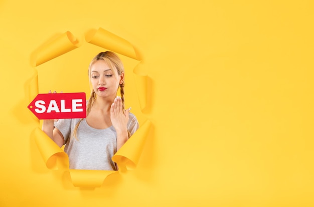 Young woman with sale inscription sign on torn yellow paper surface facial indoor shopping