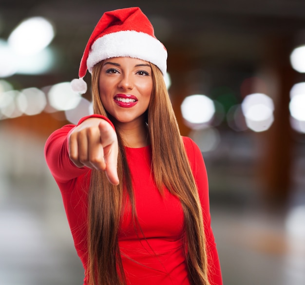 Young woman with santa hat pointing at you