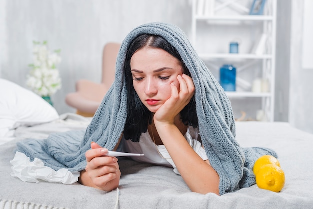 Young woman with scarf around her head checking fever with thermometer