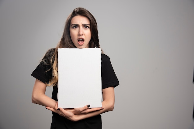 Young woman with shocked expression holding canvas. 