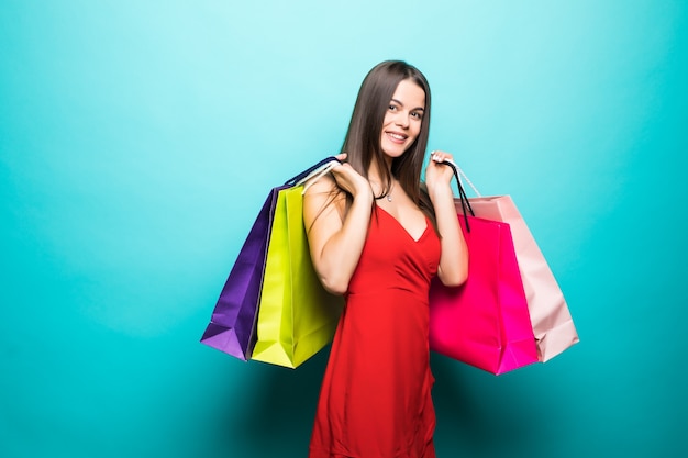 Young woman with shopping bags in red dress on blue wall