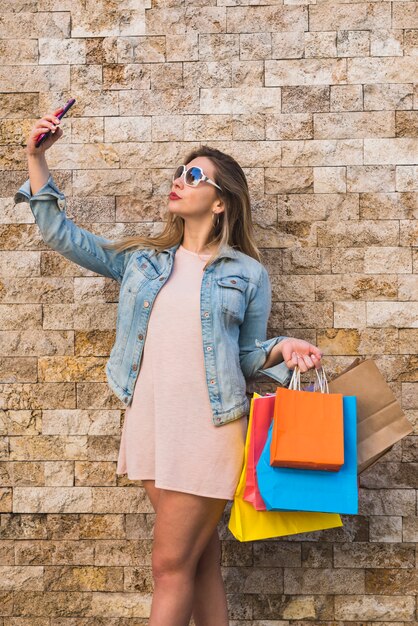 Молодая женщина с хозяйственными сумками принимая selfie