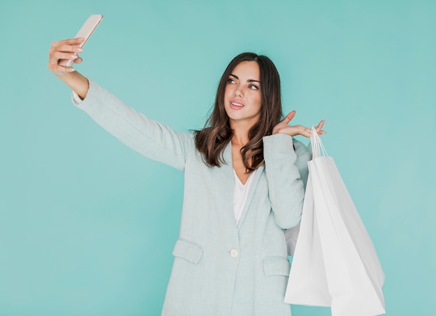 Молодая женщина с хозяйственными сумками принимая selfie
