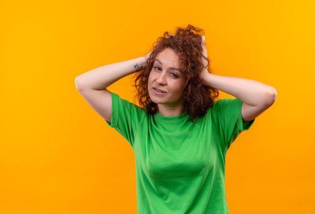 緑のTシャツの短い巻き毛の若い女性が立っている彼の髪に触れて笑顔に見える