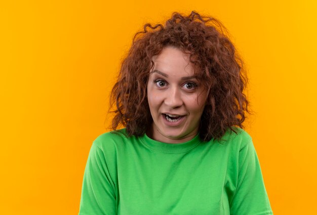 Young woman with short curly hair in green t-shirt looking surprised standing