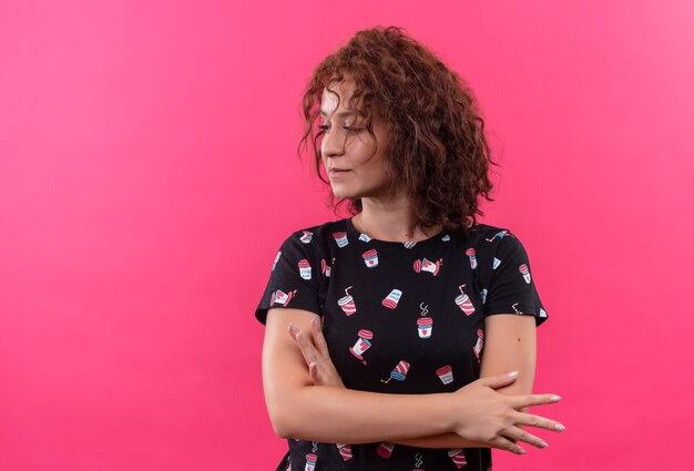 Young woman with short curly hair looking aside displeased standing over pink wall