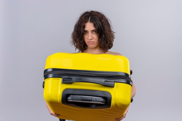 A young woman with short hair in green crop top holding yellow suitcase on a white background
