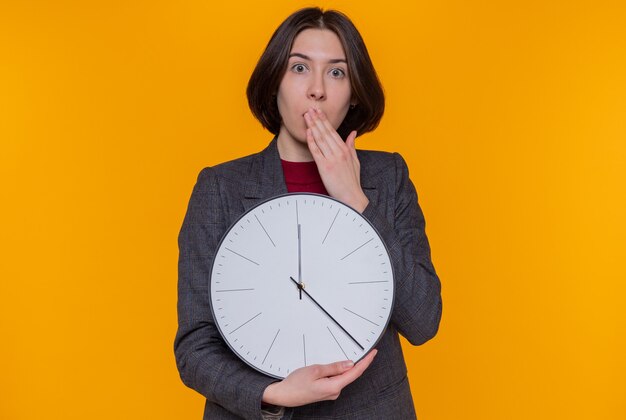 Young woman with short hair wearing grey jacket holding wall clock