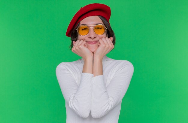 Young woman with short hair in white turtleneck wearing beret and yellow sunglasses