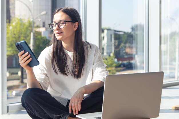 Young woman with smartphone in front of laptop screen in office