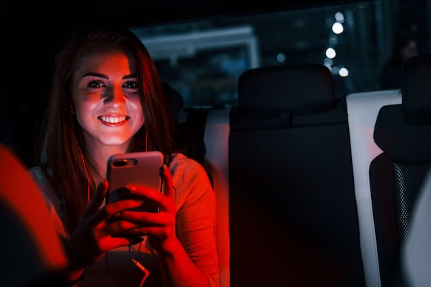 Молодая женщина со смартфоном находится внутри нового современного автомобиля.