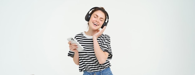Free photo young woman with smartphone listening to music dancing to her favourite song in headphones posing