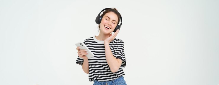 無料Photo ヘッドフォンのポーズで好きな曲に合わせて踊る音楽を聴くスマートフォンを持つ若い女性