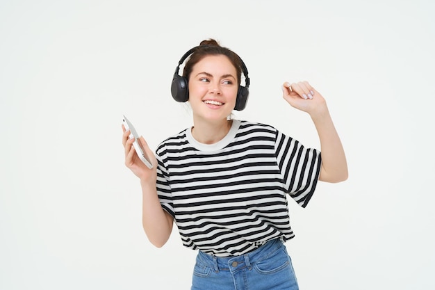 Free photo young woman with smartphone listening to music dancing to her favourite song in headphones posing