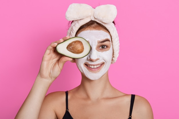 Young woman with smile holding avocado against her eyes, smiling