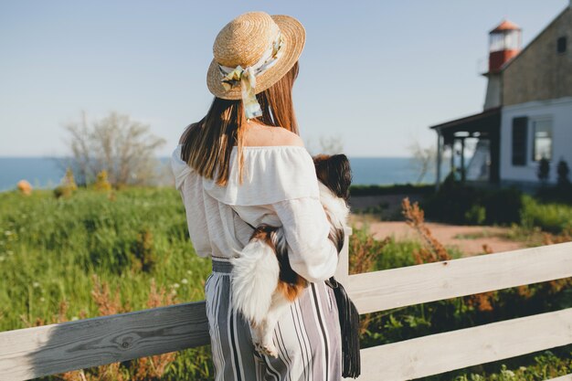 田舎のフェンスで彼女の犬と麦わら帽子を持つ若い女性