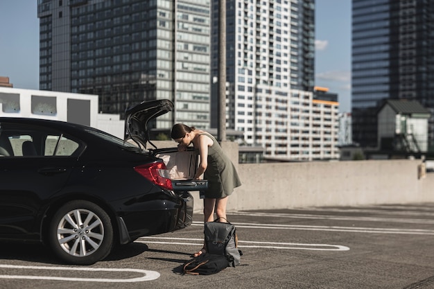 車のトランクで開いているスーツケースを持つ若い女性