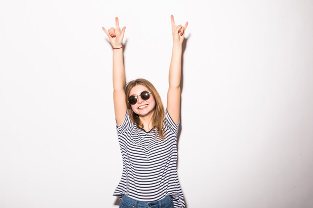 Young woman with sunglasses giving the Rock and Roll sign isolated on white wall