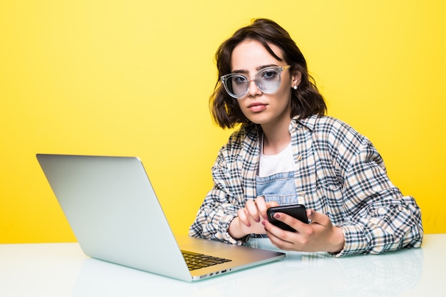 Молодая женщина в солнечных очках с руками, используя современный смартфон, работая в офисе с изолированным компьютером