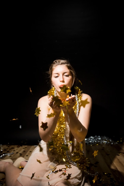 Young woman with tinsel blowing on ornament paper stars on floor 