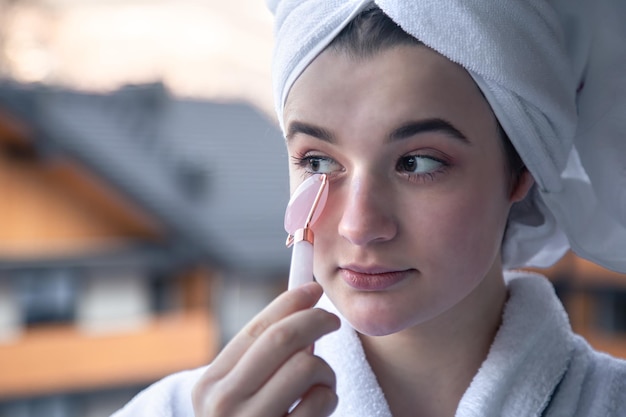 A young woman with a towel on her head is doing a massage with a facial roller