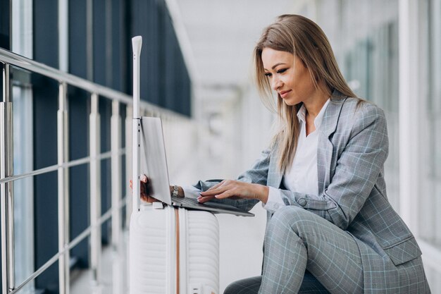 Young woman with travel bag, booking a flight on laptop in airport