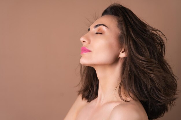 Young woman with wavy voluminous hair on a beige background with bright pink lipstick lip gloss topless bare shoulders