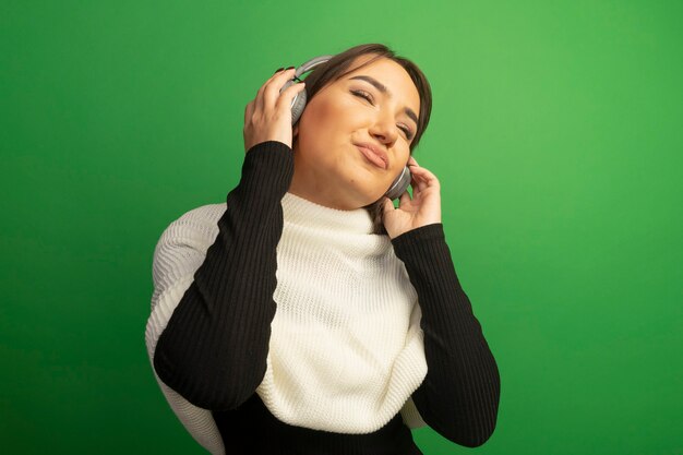 彼女の好きな音楽を楽しんでいる白いスカーフとヘッドフォンを持つ若い女性