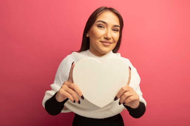 Young woman with white scarf holding cardboard heart with smile on face 