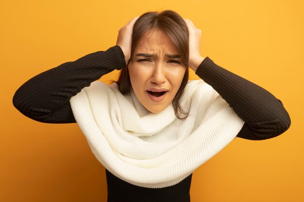 Young woman with white scarf holding hands on head shouting and yelling with annoyed expression 