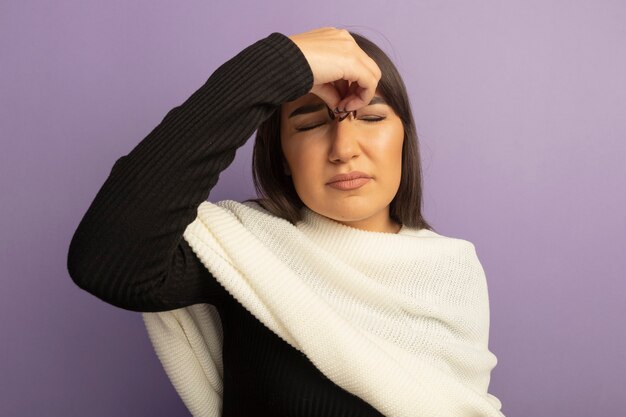 Young woman with white scarf looking tired and bored touching her nose between closed eyes 