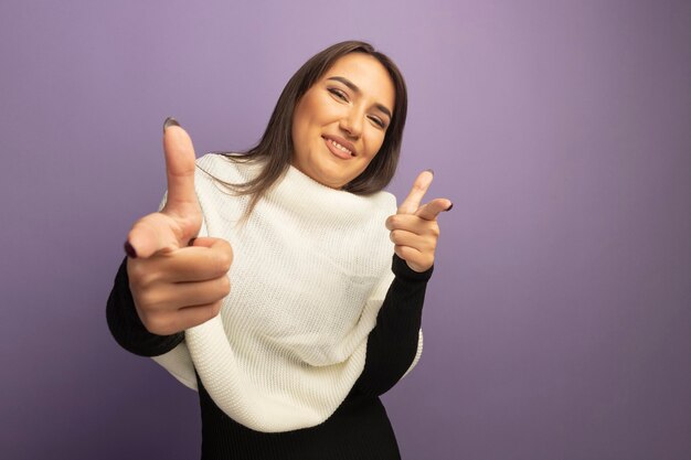 幸せで陽気な笑顔のカメラでインデックスfignersを指す白いスカーフを持つ若い女性