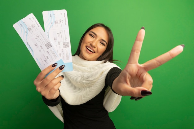 Free photo young woman with white scarf showing air tickets happy and cheerful smiling showing v-sign