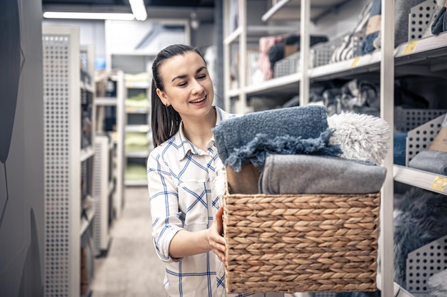 Free photo a young woman with a wicker basket full of blankets in a home improvement store