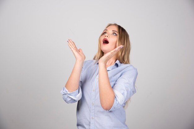 Young woman with widely opened mouth holding raised hands and looking up.