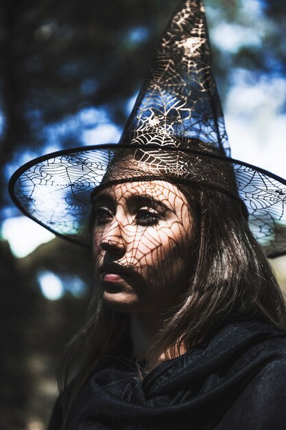 Young woman in wizard hat and cloak looking away in forest