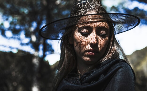 Молодая женщина в шляпе волшебника и плащ, глядя вниз в лесу