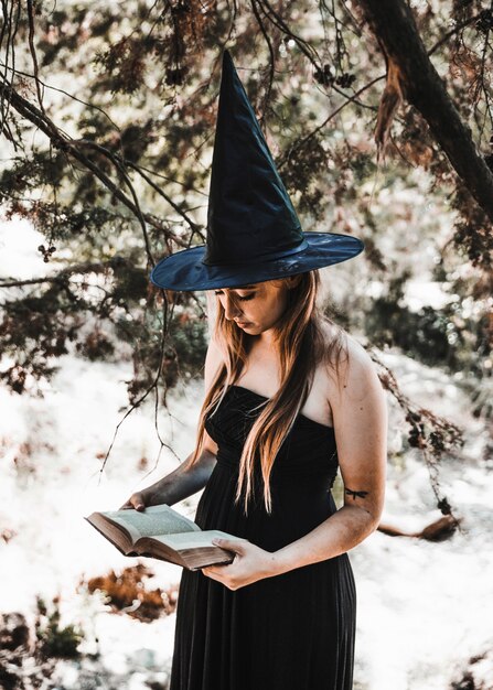 Young woman in wizard hat reading book in woods