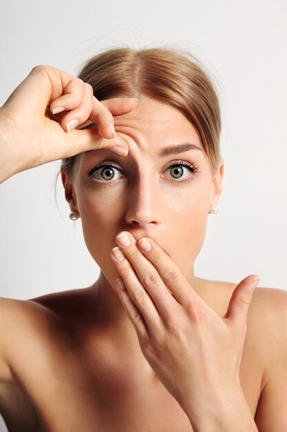 Young woman wondering that hse have first wrinkle on her forehead