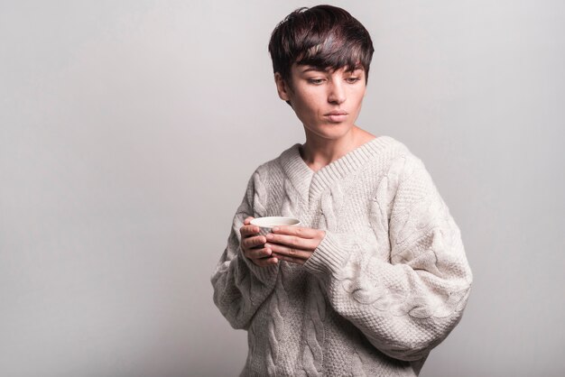 Молодая женщина в шерстяной свитер проведение чашку кофе на сером фоне
