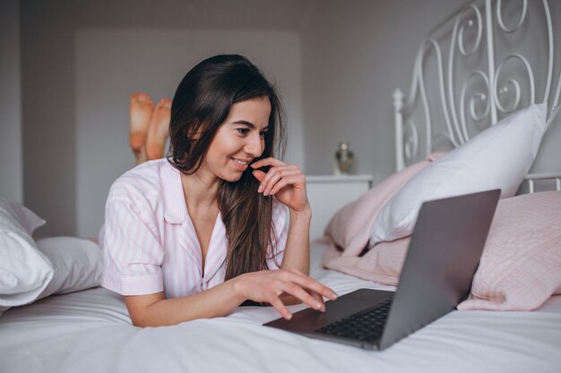 Молодая женщина работает на компьютере в постели
